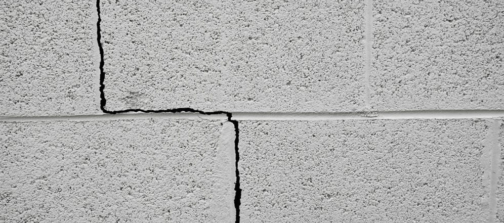 Stair‑step cracks in a concrete block foundation wall caused by foundation settling in a West Virginia home.
